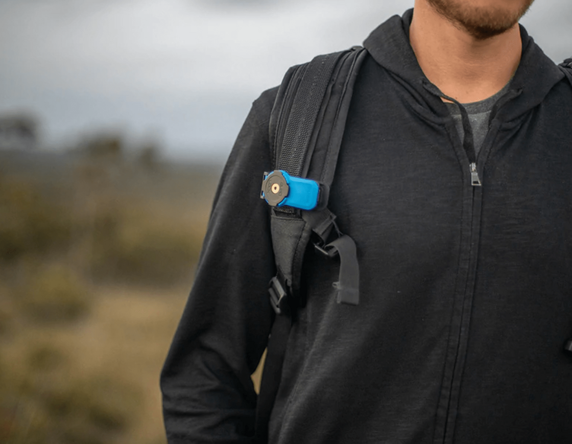 Quadlock ryggsäck/bältklämma fäst på en ryggsäcksrem, vilket möjliggör enkel och säker åtkomst till mobilen under utomhusaktiviteter.